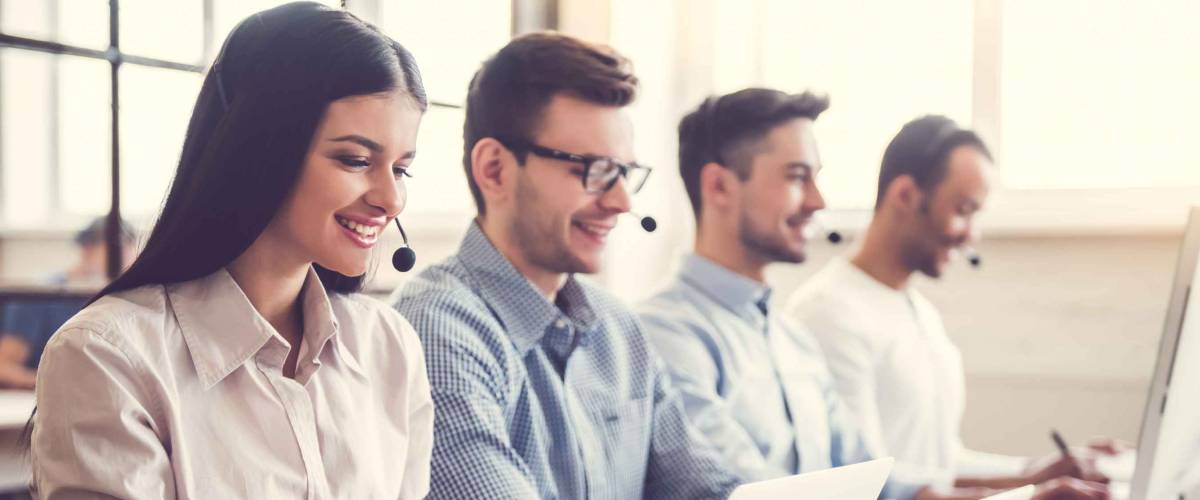 Beautiful business people in headsets are using computers and smiling while working in office