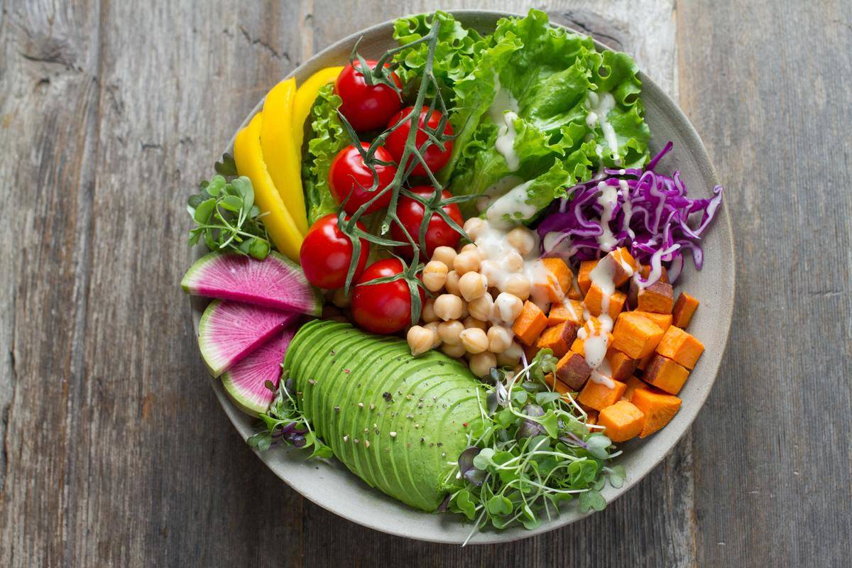 a salad with avocado, tomatoes, garbanzo beans, cabbage, sweet potato, peppers, and sprouts